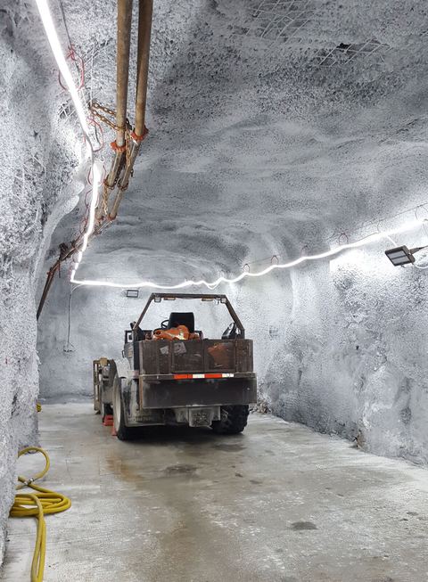 Underground mine tunnel lit by a line of LED lights with a vehicle in the foreground